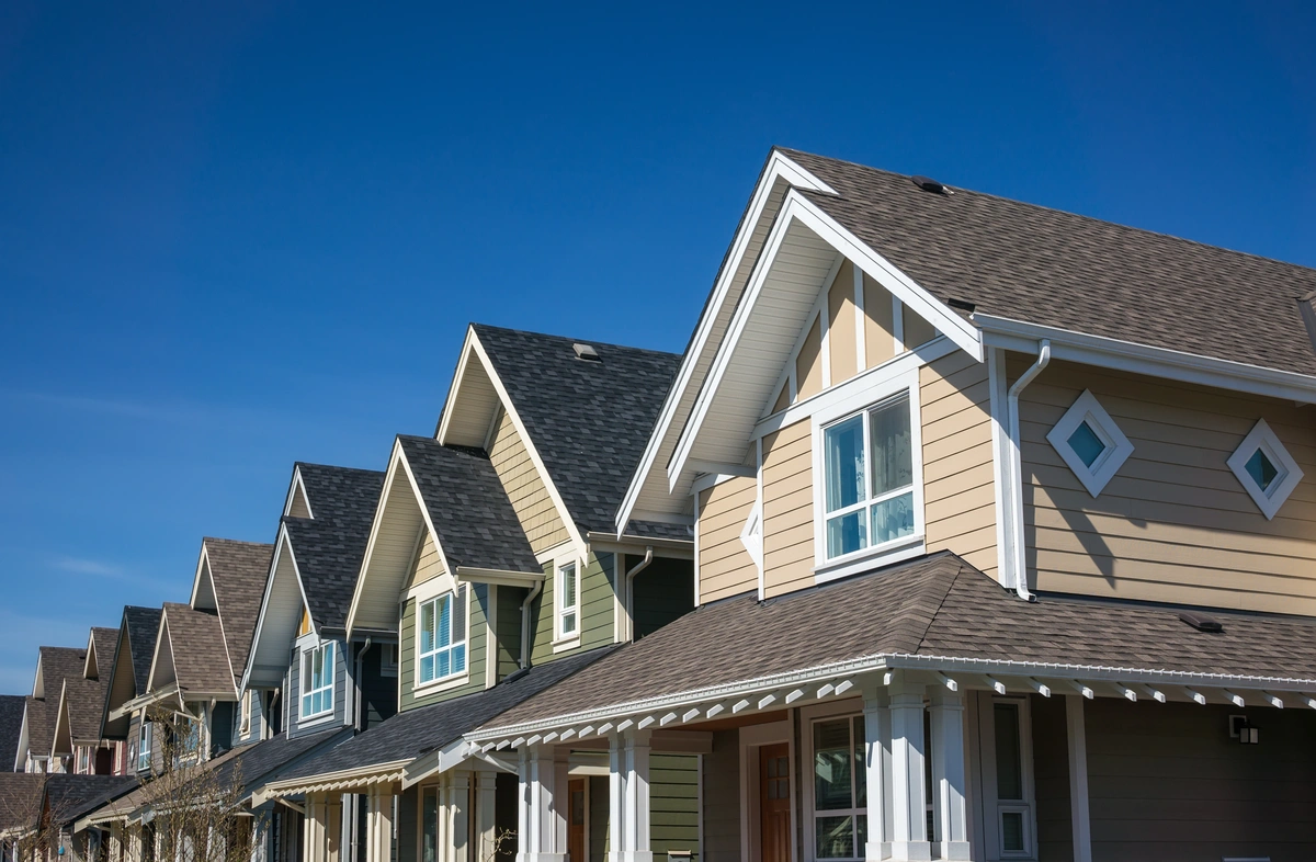 Row of modern suburban houses with gabled roofs and beige siding under a clear blue sky.