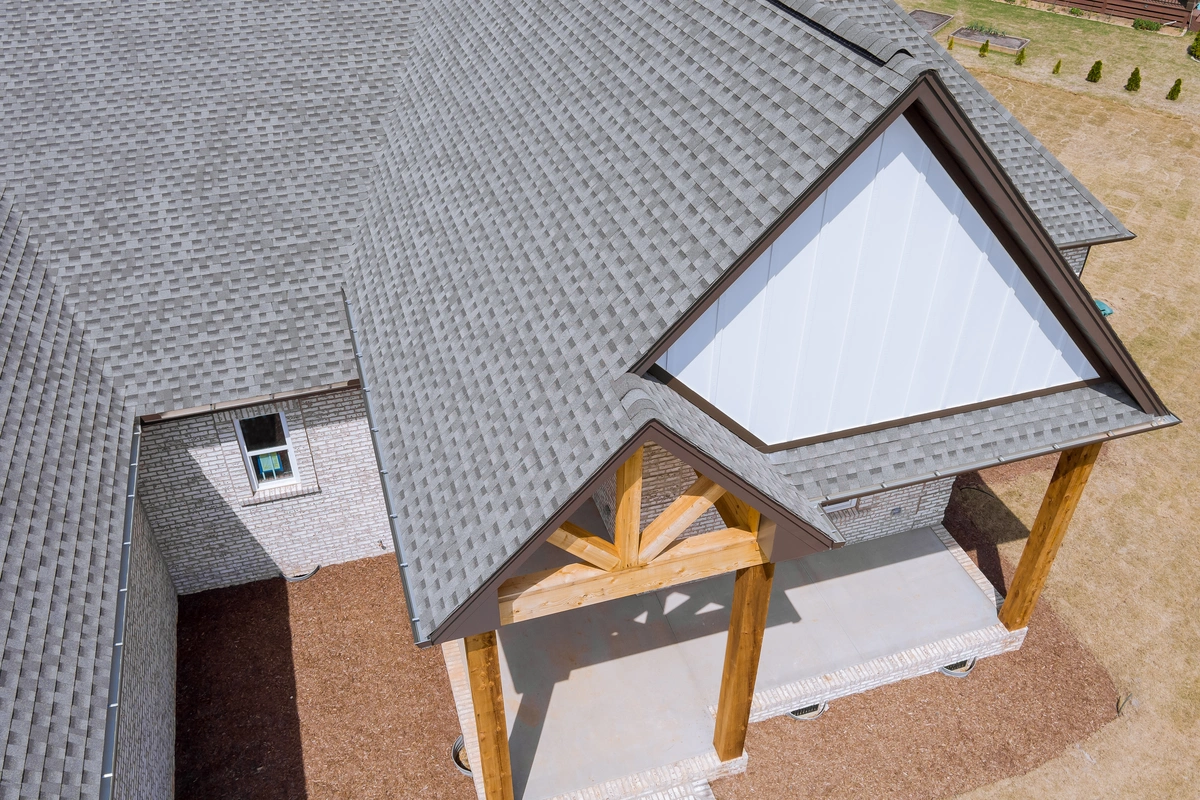 Aerial view of a houses roof with gray shingles, wooden support beams, and a covered entrance area on a mulched yard.