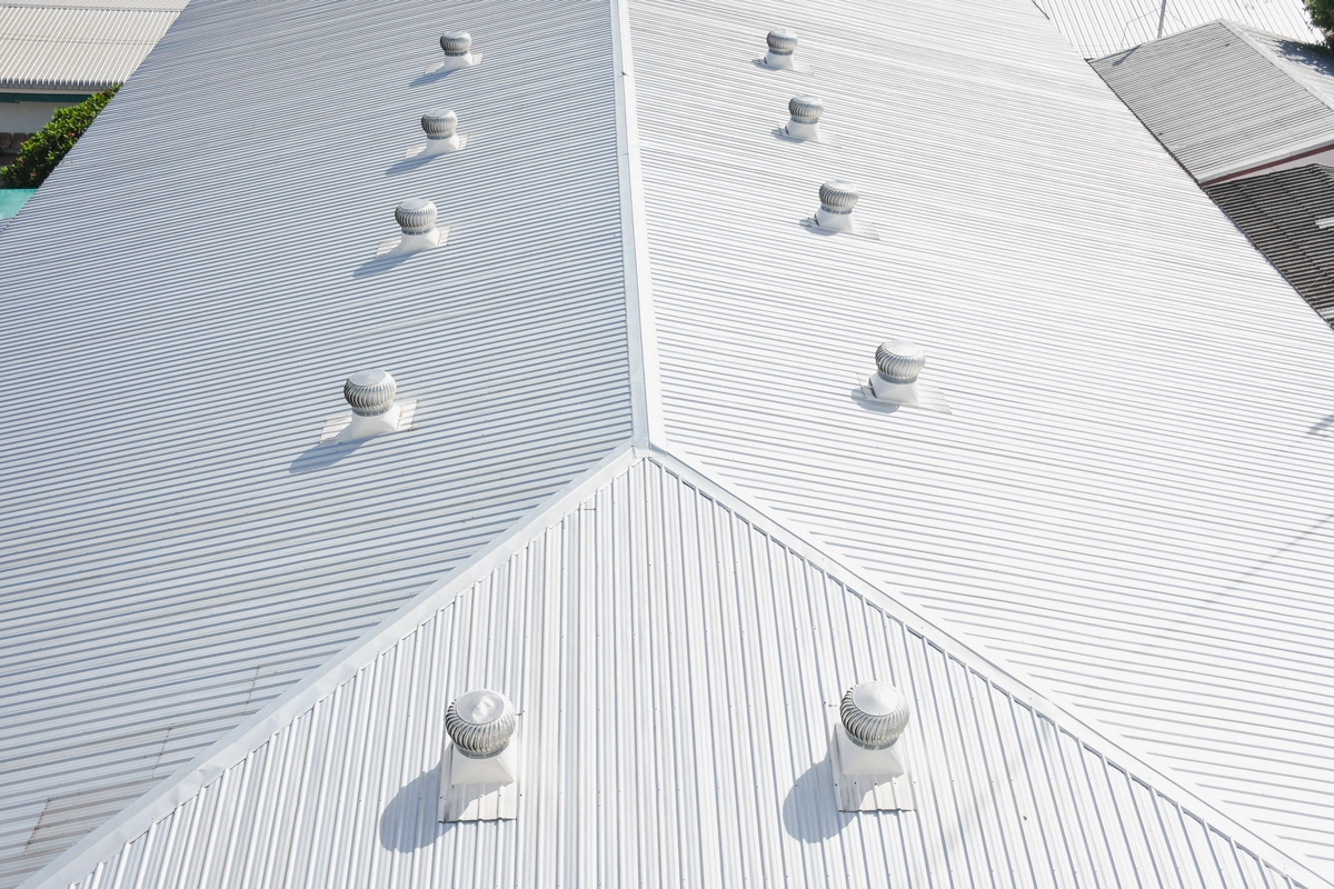 A white metal roof with multiple turbine vents evenly spaced along the ridge and slopes, photographed from above. A white metal roof with multiple turbine vents evenly spaced along the ridge and slopes, photographed from above.