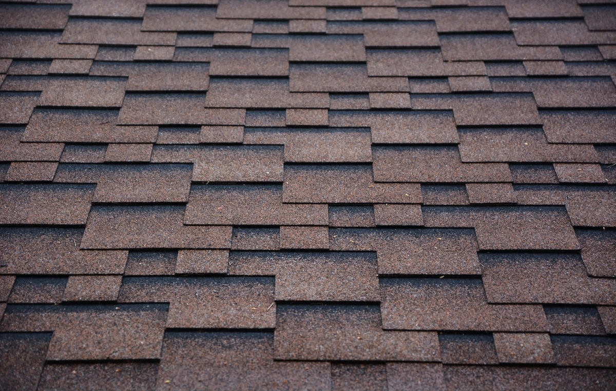 Close-up view of a roof covered with overlapping brown asphalt shingles arranged in a staggered pattern. Close-up view of a roof covered with overlapping brown asphalt shingles arranged in a staggered pattern.