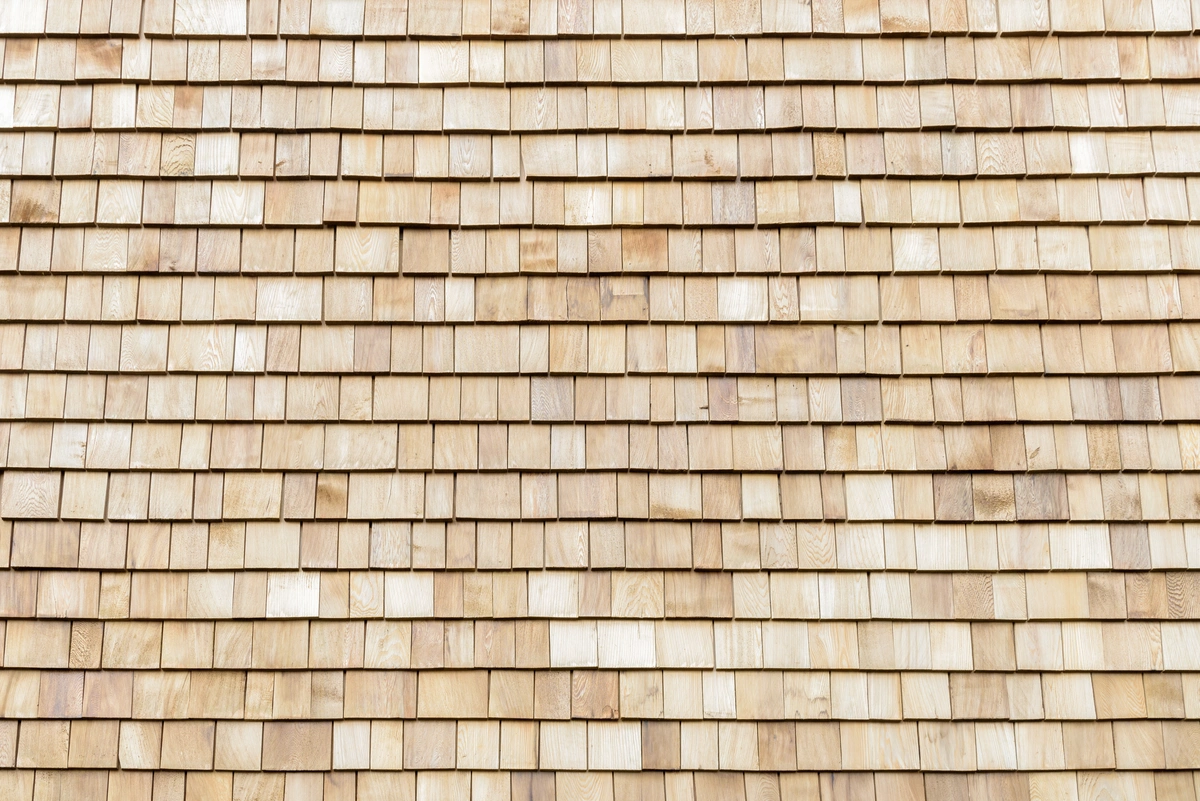 Close-up view of a wooden shingle roof showing evenly arranged, overlapping light-colored wooden tiles. Close-up view of a wooden shingle roof showing evenly arranged, overlapping light-colored wooden tiles.