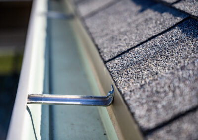 Close-up view of a clean rain gutter attached to a roof with asphalt shingles, showing a metal gutter bracket holding the gutter in place.