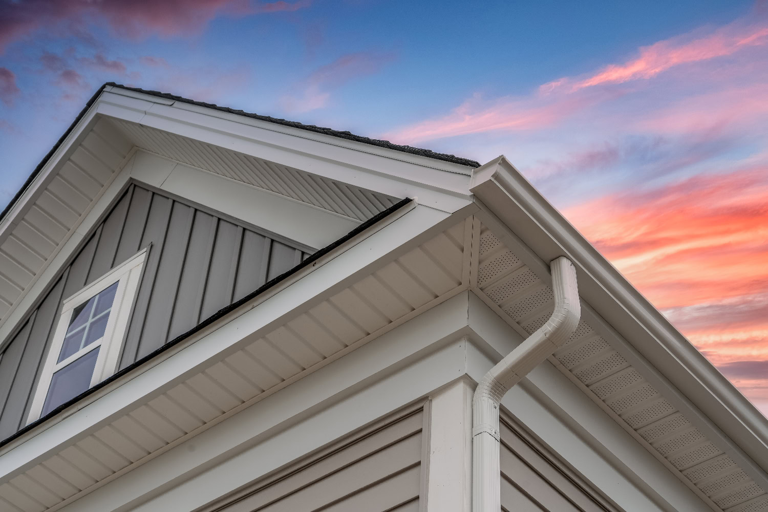 Close-up of the edge of a house with white siding and gutters, featuring a window and gable roof, set against a colorful sunset sky. Close-up of the edge of a house with white siding and gutters, featuring a window and gable roof, set against a colorful sunset sky.