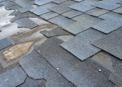 Close-up of a roof with damaged and missing asphalt shingles, exposing the underlying layers and nails.