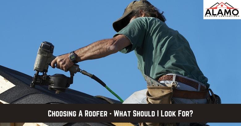 A roofer uses a nail gun to install shingles on a roof; text overlay reads, “Choosing A Roofer – What Should I Look For?” with Alamo Roofing Contractors logo in the corner. A roofer uses a nail gun to install shingles on a roof; text overlay reads, “Choosing A Roofer - What Should I Look For?” with Alamo Roofing Contractors logo in the corner.