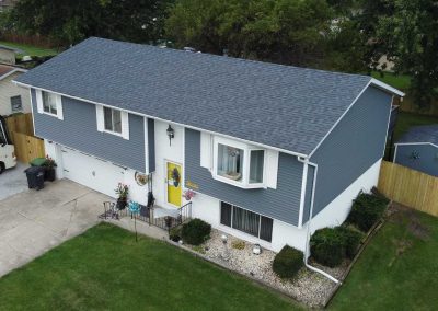 A two-story suburban house with grey siding, white trim, a yellow front door, and a well-kept yard with decorative rocks and grass.